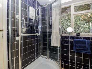A shower with sliding glass doors and blue tiled walls next to a window with a towel rack and blue towels at Small Piece in Porlock