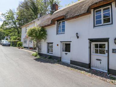 A street view of white cottages with thatched and tiled roofs and parked cars at Small Piece in Porlock