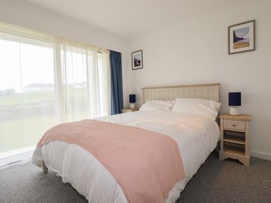 A bedroom with a double bed and pink blanket between two bedside tables with lamps at 7 Europa Court Mawgan Porth