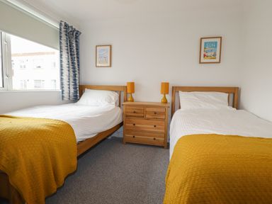 A bedroom with two single beds with yellow blankets and white pillows a wooden dresser and two framed pictures at 7 Europa Court in Mawgan Porth
