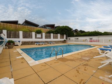 An outdoor swimming pool with several lounge chairs around it at 7 Europa Court in Mawgan Porth