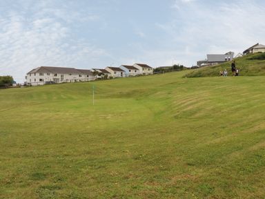 A grassy hill with a golf hole flag and houses in the background at 7 Europa Court in Mawgan Porth