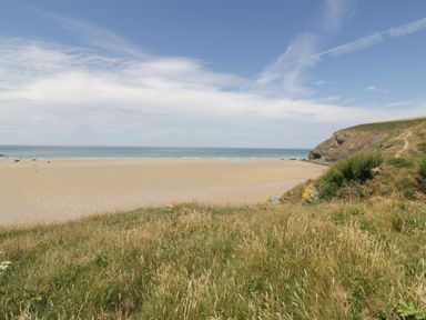 A sandy beach with distant people grassy dunes and a rocky hill at 7 Europa Court in Mawgan Porth