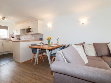 An open plan living space with a kitchen area a dining table with chairs and a sofa at 7 Europa Court in Mawgan Porth