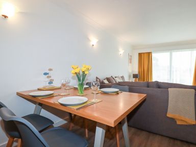 A dining table with plates glasses and flowers next to a sofa in a living room at 7 Europa Court in Mawgan Porth