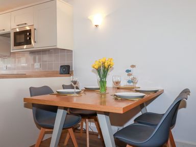 A dining area with a wooden table set for four with plates wine glasses and yellow flowers on the table at 7 Europa Court in Mawgan Porth