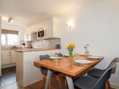 A dining table set with plates and glasses next to a kitchen area at 7 Europa Court in Mawgan Porth