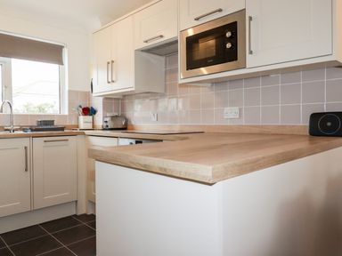 A kitchen with white cabinets wooden countertops a microwave toaster and utensils at 7 Europa Court Mawgan Porth