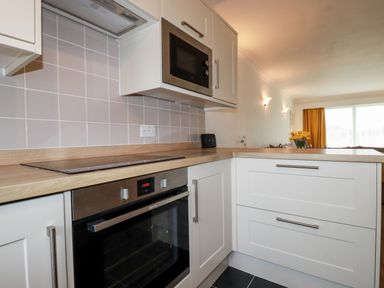 A kitchen area with white cabinets a built-in oven a microwave and a wooden countertop at 7 Europa Court in Mawgan Porth