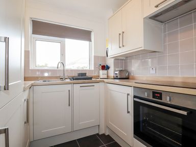 A kitchen with white cabinets a sink toaster oven and utensils at 7 Europa Court in Mawgan Porth