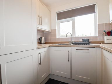A kitchen corner with white cabinets wooden countertops a window a kettle a sink a stovetop and utensil holder at 7 Europa Court in Mawgan Porth