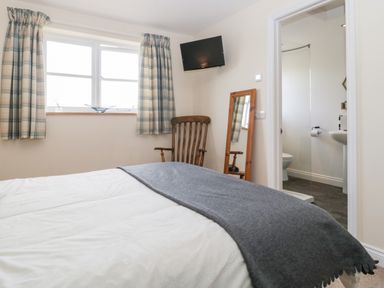 A bedroom with a bed a wooden chair a wall-mounted tv a standing mirror and an en suite bathroom at The Coal House at Mendip View in Wedmore