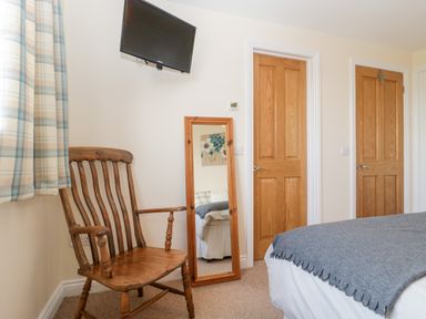 A bedroom with a wooden chair a wall mounted television a standing mirror and two wooden doors at The Coal House at Mendip View Wedmore