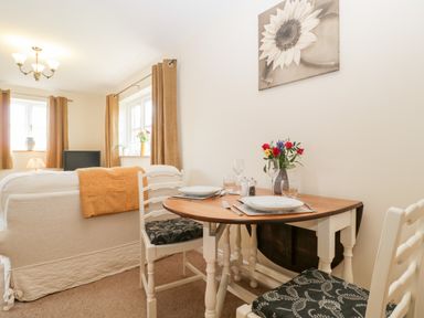 A dining area with a small table set for two and a sofa with an orange throw at The Coal House at Mendip View in Wedmore