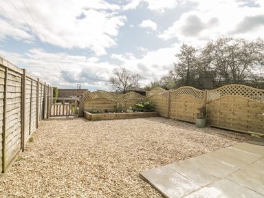 A gravel yard with wooden fences and a small garden bed with plants at The Coal House at Mendip View in Wedmore
