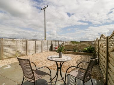A small outdoor patio with two chairs and a table with flowers fenced garden area at The Coal House at Mendip View Wedmore