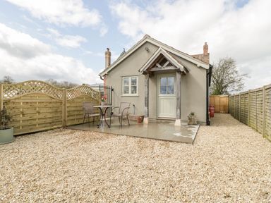 A small house with a gravel yard a patio with table and chairs and wooden fences at The Coal House at Mendip View in Wedmore