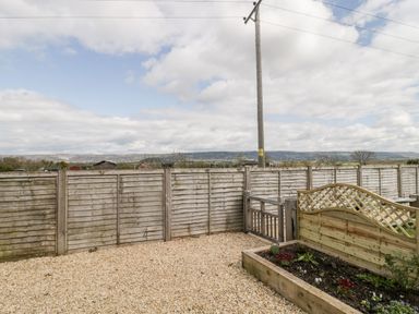 A fenced backyard with gravel ground and a raised wooden flower bed at The Coal House at Mendip View in Wedmore