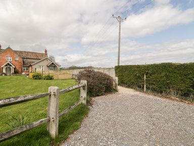 A gravel pathway next to a wooden fence and hedge with a brick house and garden in the background at The Coal House at Mendip View in Wedmore