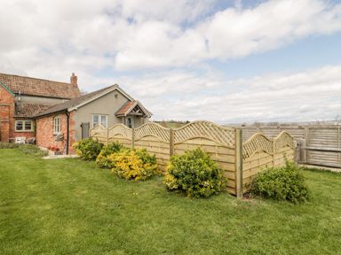 A garden with bushes and a wooden fence next to a brick and plaster house at The Coal House at Mendip View in Wedmore