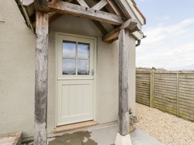An exterior wooden door with glass panels under a wooden porch with a gravel path and wooden fence at The Coal House at Mendip View Wedmore