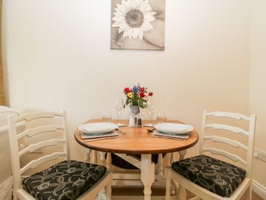 A small dining area with a round wooden table set for two with plates glasses cutlery and flowers on the table at The Coal House at Mendip View in Wedmore