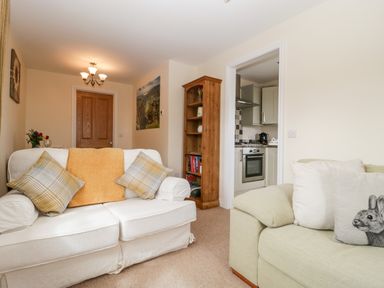 A living room with two sofas and a wooden bookshelf next to a kitchen doorway at The Coal House at Mendip View in Wedmore