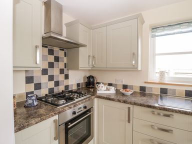 A kitchen with gas stove oven grey cabinets and tiled backsplash by a window at The Coal House at Mendip View in Wedmore