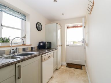 A kitchen with a sink, dishwasher, refrigerator, microwave, clock, and a door leading outside at The Coal House at Mendip View in Wedmore