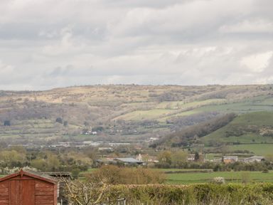 A rural landscape with hills trees and fields and wooden sheds in the foreground at The Coal House at Mendip View in Wedmore