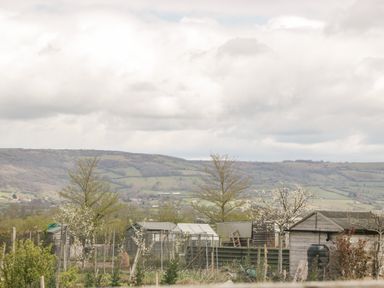 A garden area with several wooden sheds trees and hills in the background at The Coal House at Mendip View in Wedmore