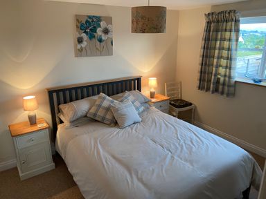A bedroom with a bed between two bedside tables with lamps and a window with checked curtains at The Coal House at Mendip View in Wedmore