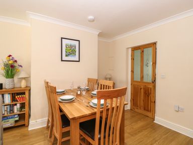 A dining room with a wooden table set for six with plates and glasses a wooden bookshelf with books and flowers a wooden door and a framed picture on the wall at Inglewood in Keswick