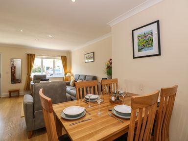 A dining table set with plates glasses and cutlery next to a living room with sofas and a window at Inglewood in Keswick
