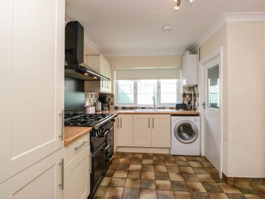 A kitchen with cream cabinets a black stove a washing machine under the countertop and a window above the sink at Inglewood in Keswick
