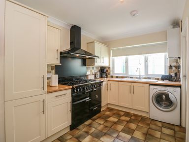 A kitchen with cream cabinets black stove washing machine and window in Inglewood Keswick
