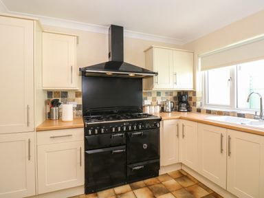 A kitchen with cream cabinets a black stove and oven a countertop with kitchen utensils and coffee maker and a window with a sink at Inglewood in Keswick