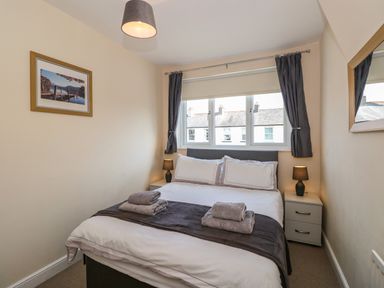 A bedroom with a double bed bedside tables lamps a framed picture and curtained windows at Inglewood in Keswick