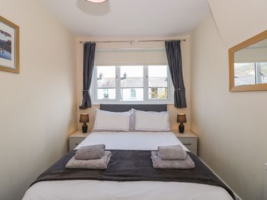 A bedroom with a bed with folded towels on top bedside tables with lamps a window with curtains and a mirror on the wall at Inglewood in Keswick