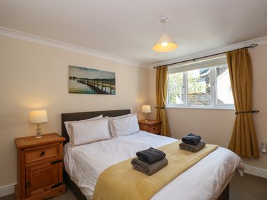 A bedroom with a double bed two bedside tables lamps a window with yellow curtains and a painting on the wall at Inglewood in Keswick