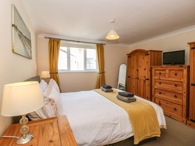 A bedroom with a bed with folded towels on a yellow blanket next to wooden wardrobes and a chest of drawers at Inglewood in Keswick