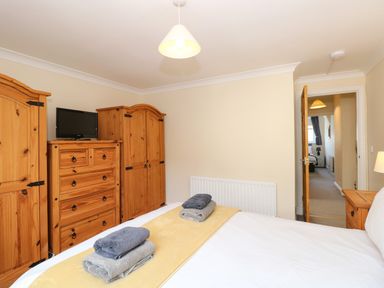 A bedroom with a bed, folded towels on the bed, wooden wardrobes, a chest of drawers with a TV, and an open door leading to a hallway at Inglewood in Keswick