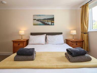 A bedroom with a double bed two bedside tables with lamps folded towels on the bed and a window with curtains at Inglewood in Keswick