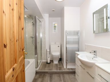 A bathroom with a wooden door a shower enclosure a toilet a towel radiator and a sink with a vanity cabinet at Inglewood in Keswick