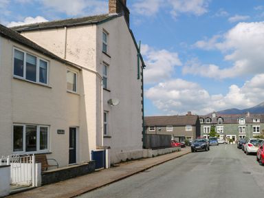 A street with parked cars and residential buildings under a partly cloudy sky at Inglewood in Keswick