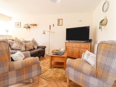 A living room with a TV on a wooden cabinet two armchairs and a sofa at Varley Villa in Newtown