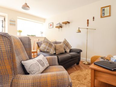 A living room with a plaid armchair a black leather sofa cushions a standing lamp and wooden shelves on the wall at Varley Villa in Newtown