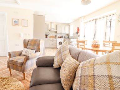 A living room with a sofa and armchair next to an open kitchen and dining table at Varley Villa in Newtown