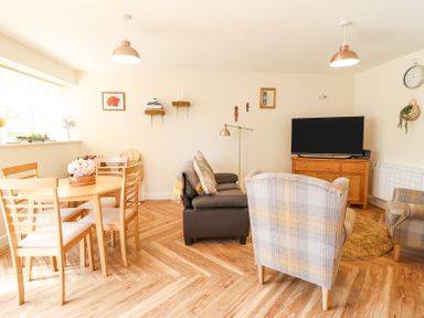 A living room with a round dining table and chairs a sofa armchairs and a television on a wooden cabinet at Varley Villa in Newtown