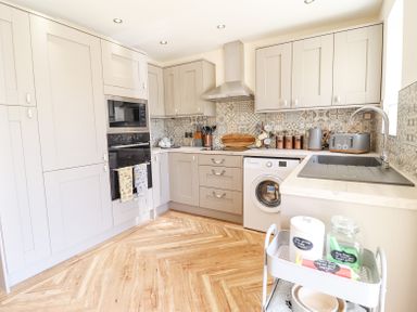 A kitchen with gray cabinets patterned tile backsplash wooden cutting boards a washing machine and a sink at Varley Villa in Newtown